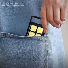 A hand slides the compact black LED keychain light with four yellow squares into the back pocket of blue jeans.