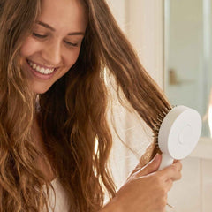 Hand pressing the quick-release button on the Self-Cleaning Hair Brush to remove trapped hair.