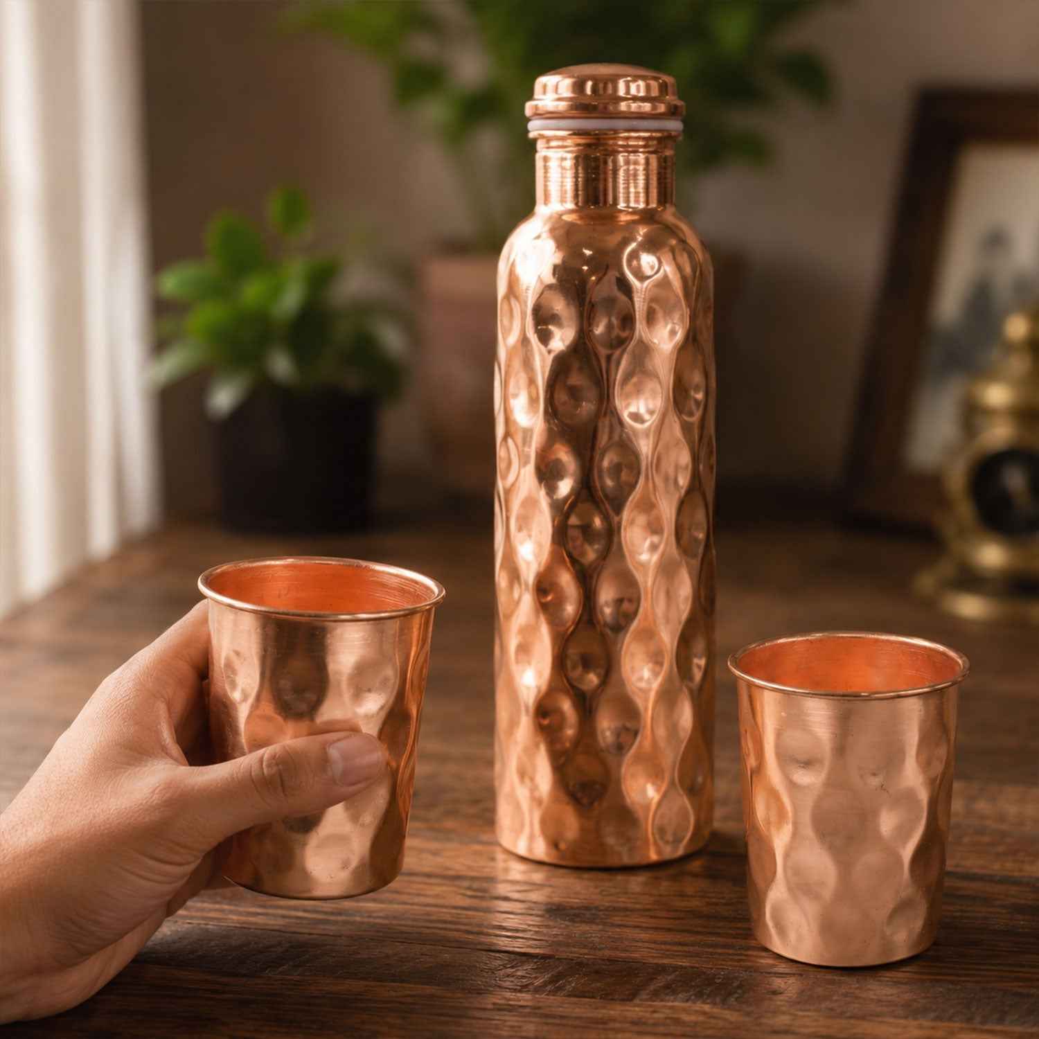 Diamond cut copper water bottle set with two matching glasses on a light background.