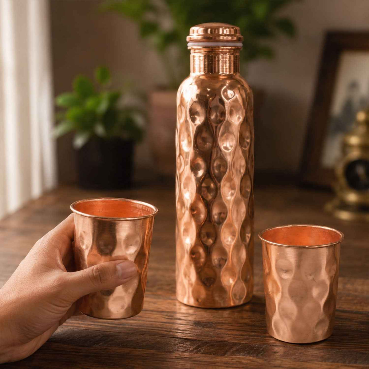 Diamond cut copper water bottle set with two matching glasses on a light background.